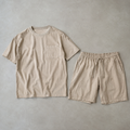 a coordinated beige men's two piece outfit consisting of a short sleeve crew neck t-shirt with one chest patch pocket and matching drawstring shorts, both fully visible side by side
