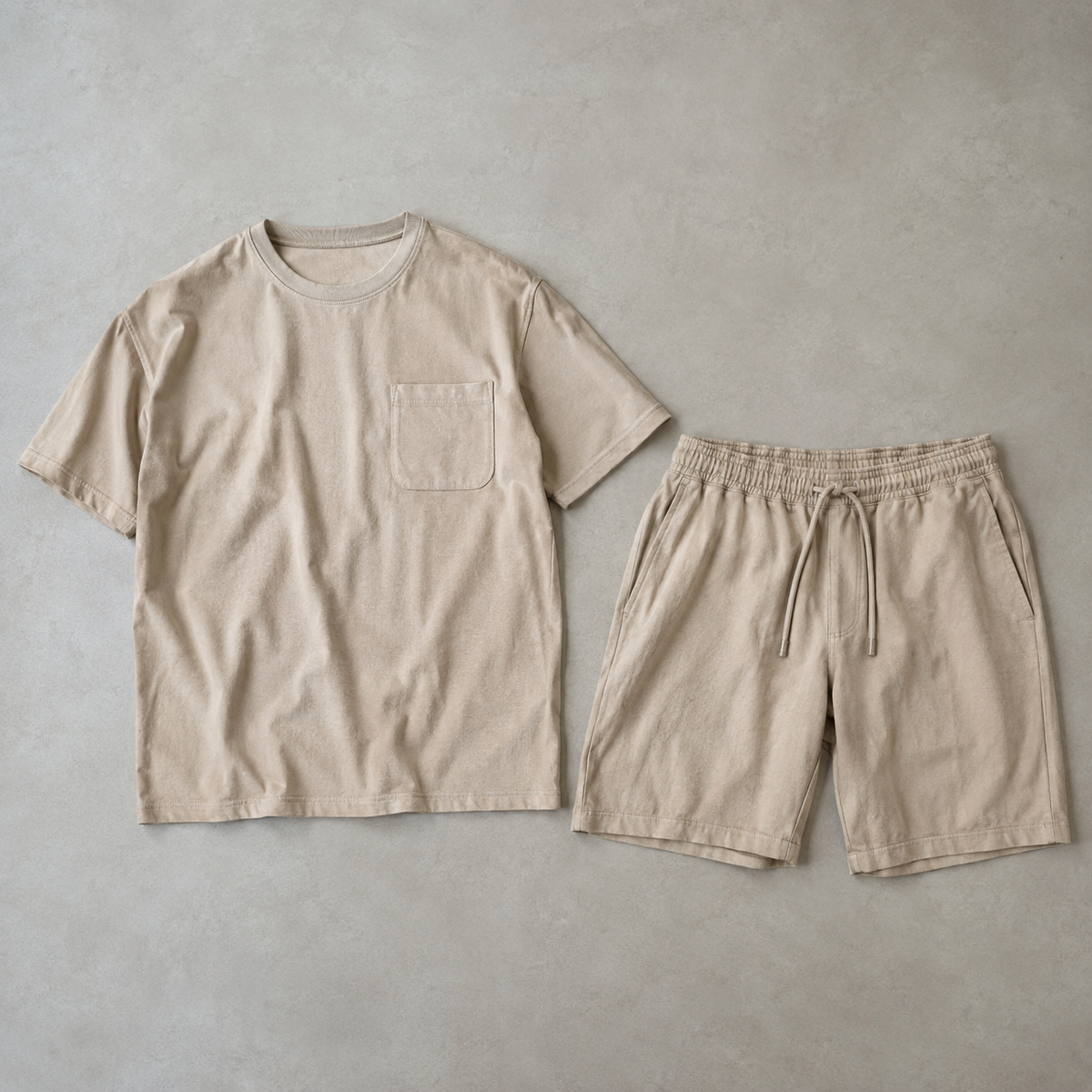 a coordinated beige men's two piece outfit consisting of a short sleeve crew neck t-shirt with one chest patch pocket and matching drawstring shorts, both fully visible side by side